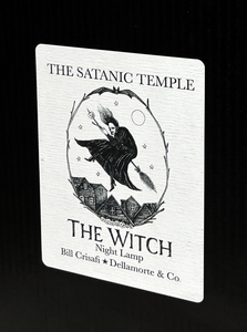 A white rectangular product card or label with black printed text reading 'THE SATANIC TEMPLE' and 'THE WITCH Night Lamp,' plus the names Bill Crisafi and Dellamorte & Co., shown against a black background.