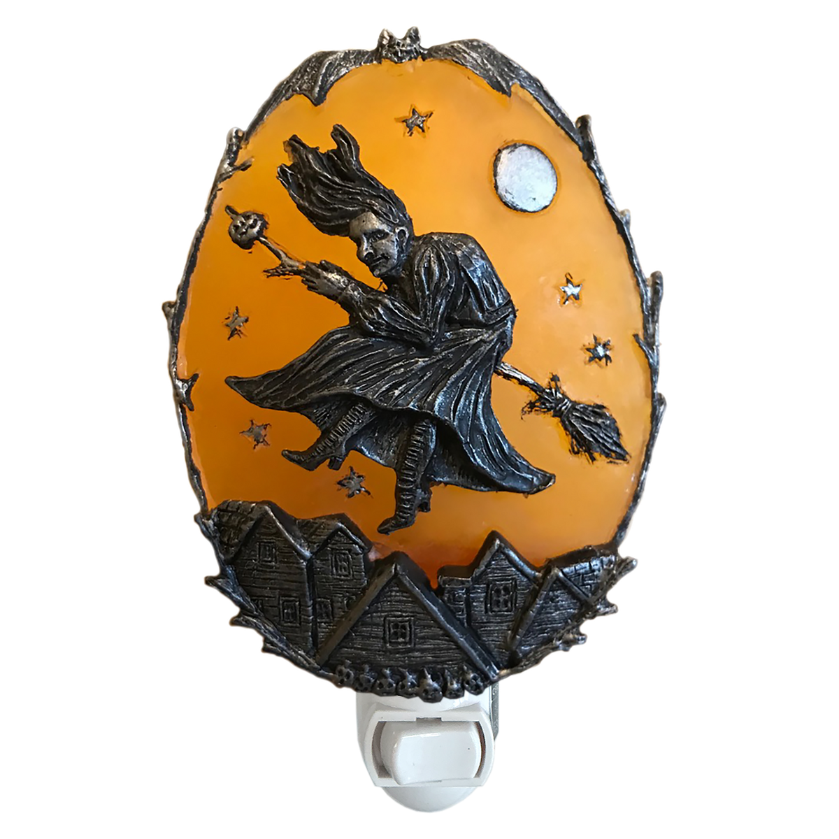 A Halloween-themed night light featuring an orange oval panel with a black metal relief of a witch riding a broomstick under a full moon, above small haunted houses, with a white switch base.