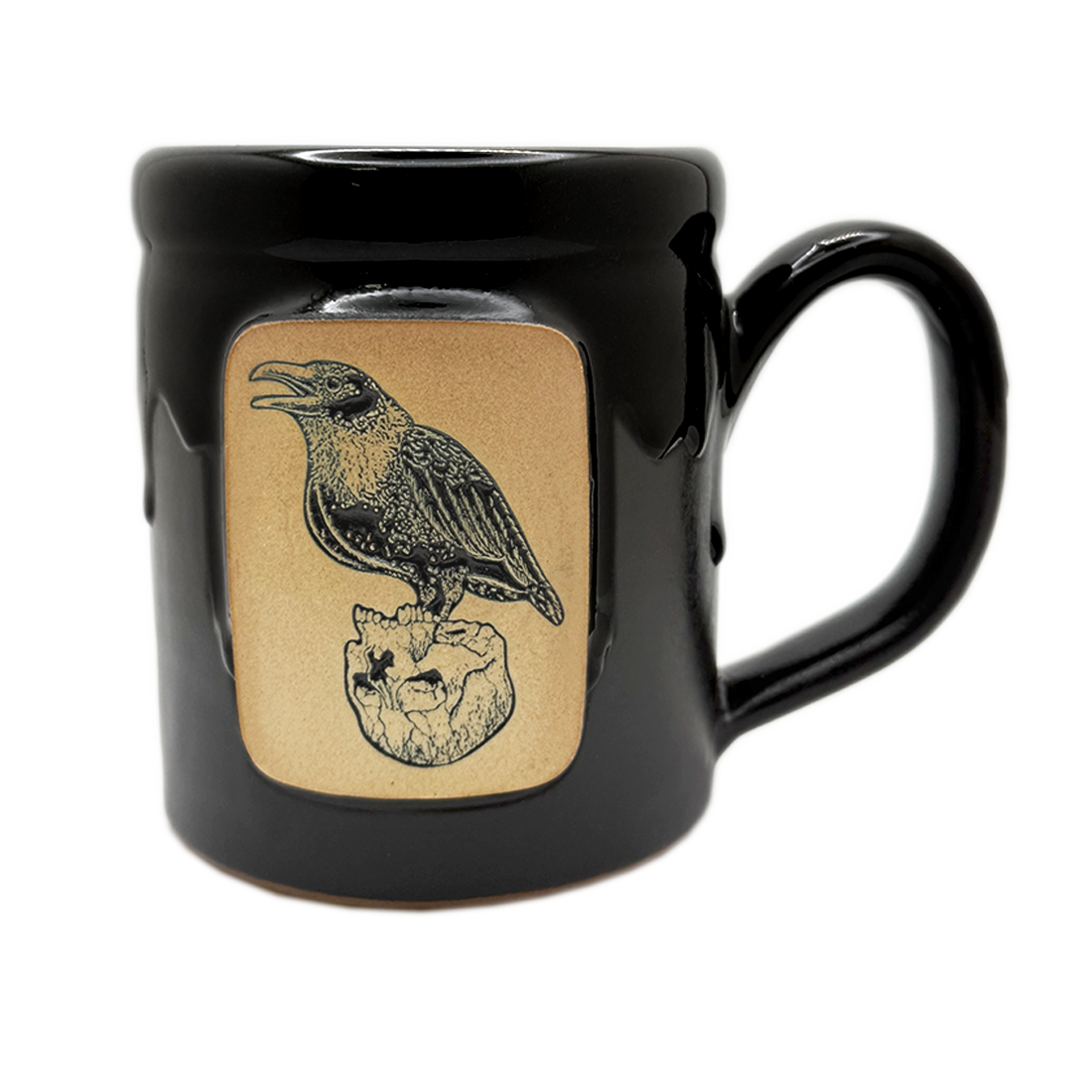 A glossy black ceramic mug featuring a square tan panel on the front with a black illustration of a raven perched on a skull.