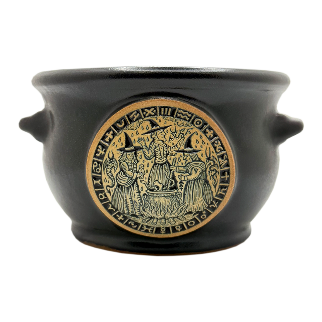 A black ceramic cauldron-shaped pot with side handles and a circular embossed gold-toned relief depicting three wizards around a cauldron, set against a plain white background.